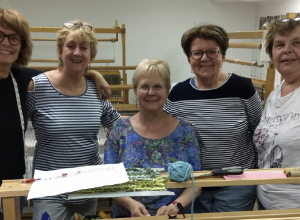 Groupe de femmes souriantes réunies devant des machines à tisser.