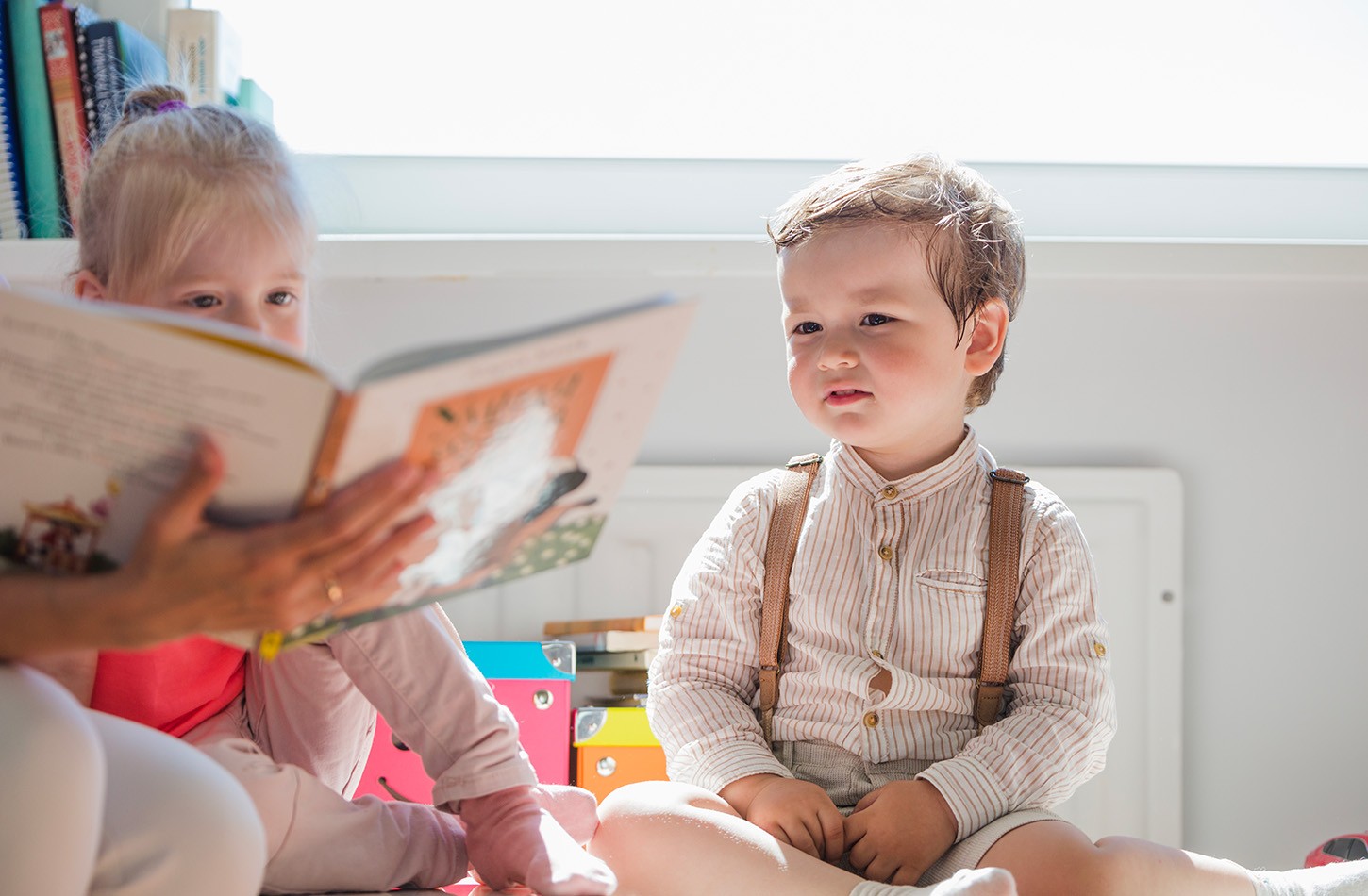 Deux enfants regardant un livre ouvert tenu par un adulte, caché dans la photo.