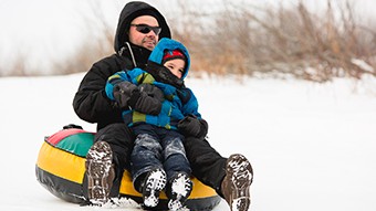 Un papa et son enfant glissent sur la neige sur une chambre à air.