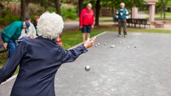 Vue de derrière d'une femme âgée lançant une boule sur un terrain de pétanque.