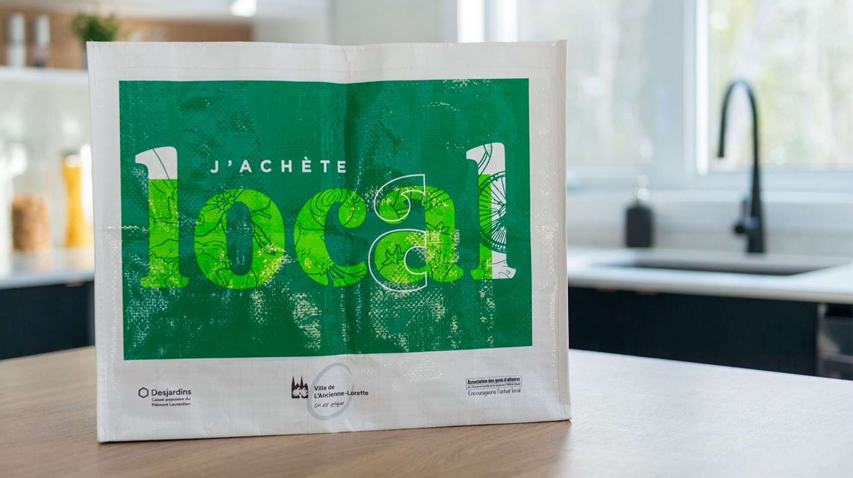 Sac réutilisable sur un comptoir de cuisine avec la mention J'achète local, aux couleurs de la Ville de L'ancienne-Lorette.