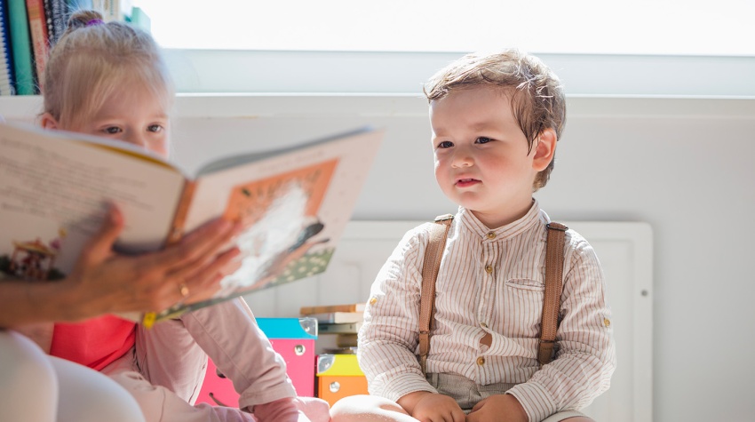 Deux enfants regardant un livre ouvert tenu par un adulte, caché dans la photo.